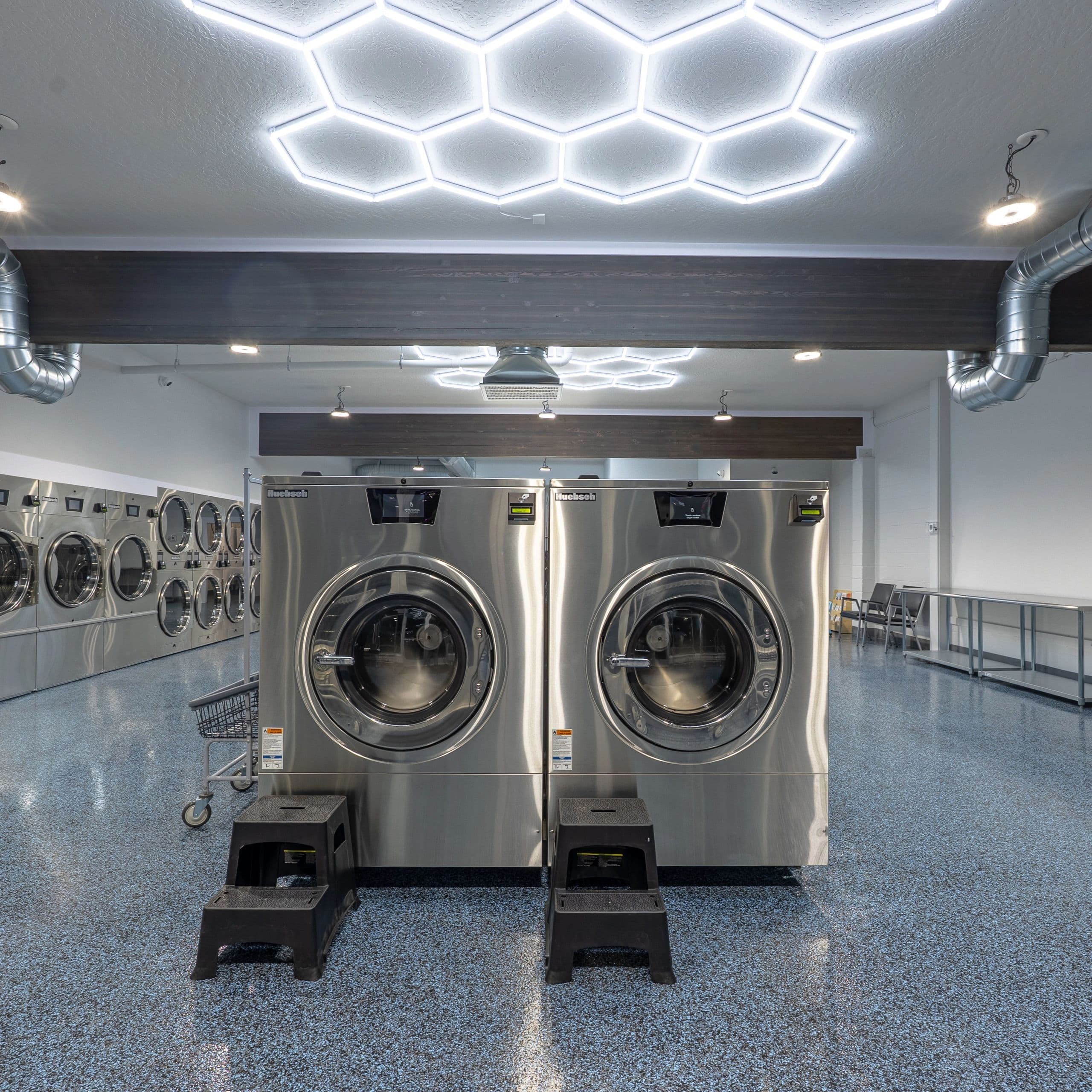 Inside 123 Laundry — a clean, modern laundromat with stainless commercial washers and honeycomb LED ceiling lighting