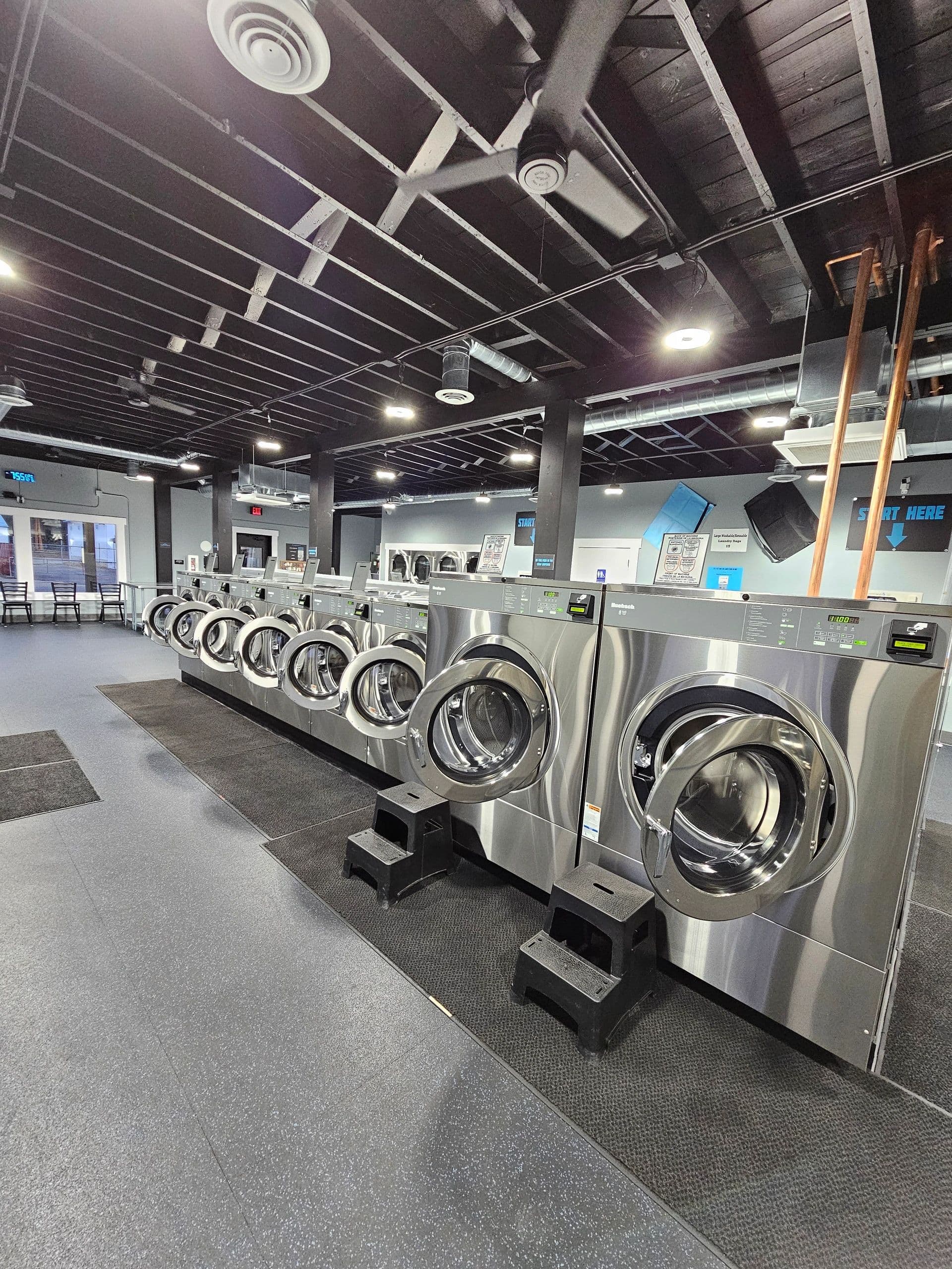 A long row of stainless commercial front-load washers at 123 Laundry